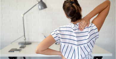 Woman sitting at a desk and reaching for her upper back